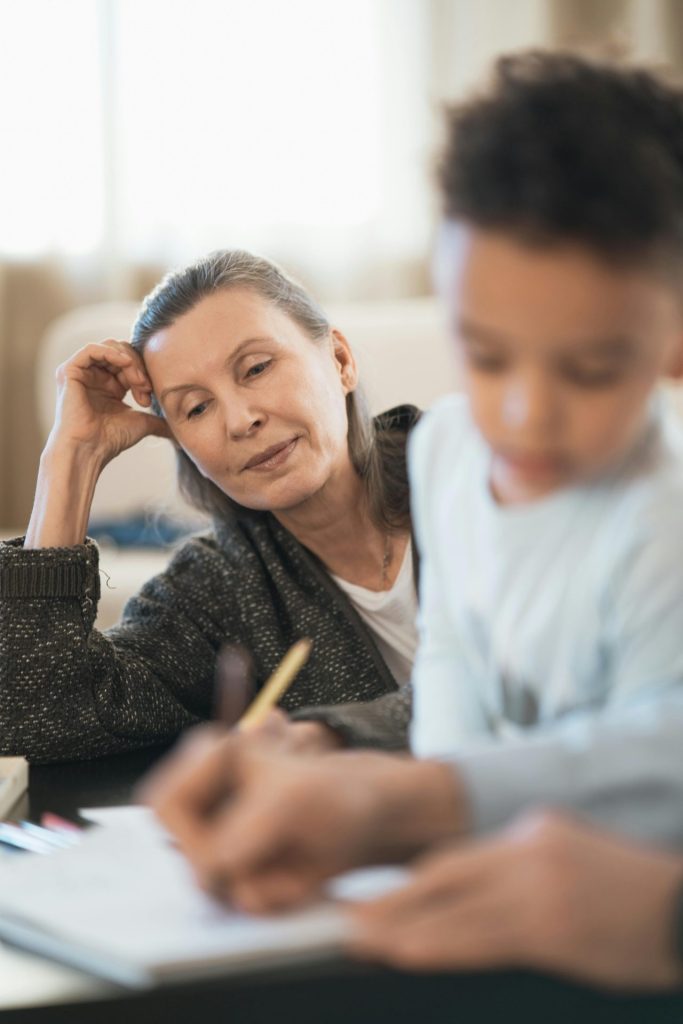 A senior woman watches her grandchild drawing indoors, sharing a precious family moment.