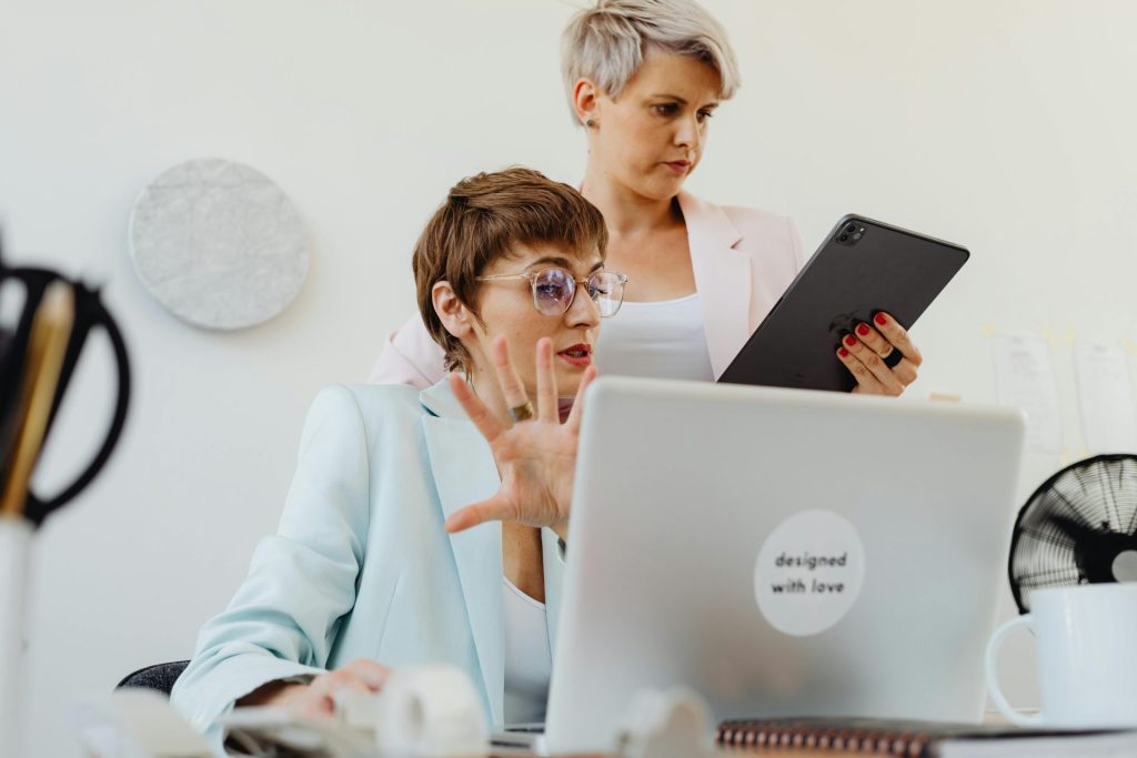Two businesswomen collaborating with a laptop and tablet in a modern office environment.